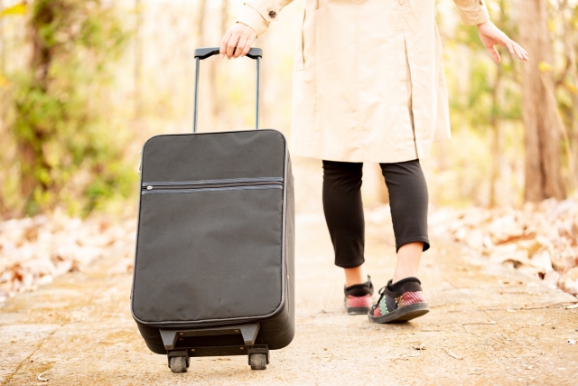 黒いスーツケースを引くレギンスとスカートをはいた女性の足元