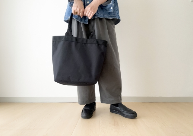 黒のトートバッグを手に持つ女性の足元