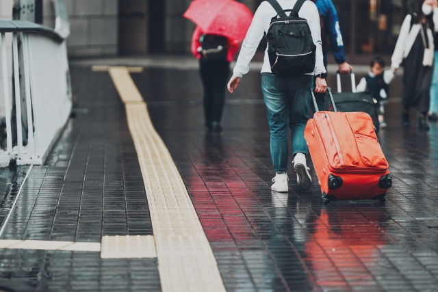 黒いリュックを背負い雨が降った道でキャリーケースを引く旅行客