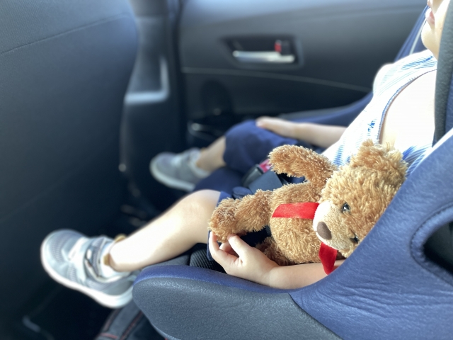 クマのぬいぐるみを抱えながらチャイルドシートに座って眠る子供